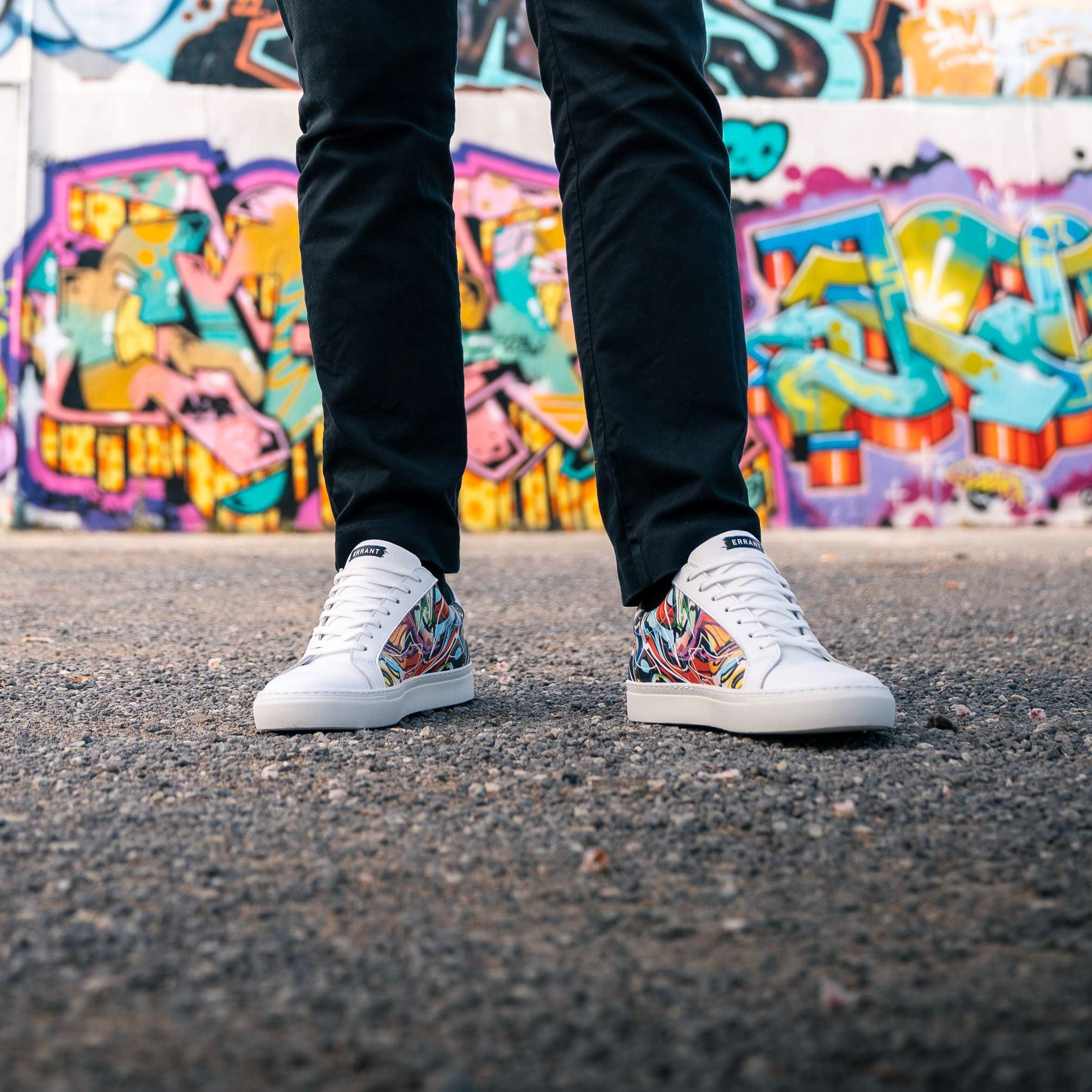 En person iført farverige sneakers står foran en væg med graffiti.
