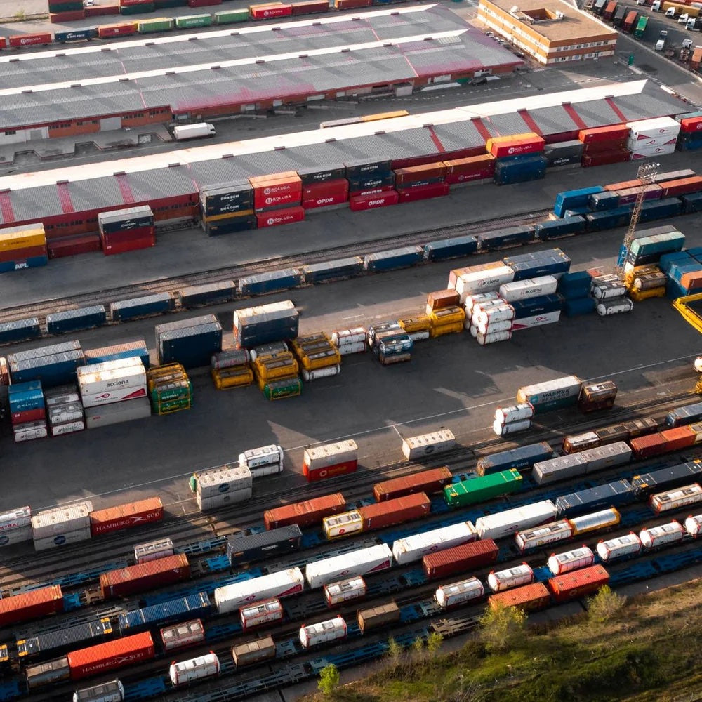 Luftfoto af en travl containerterminal med mange farverige containere stablet i rækker.