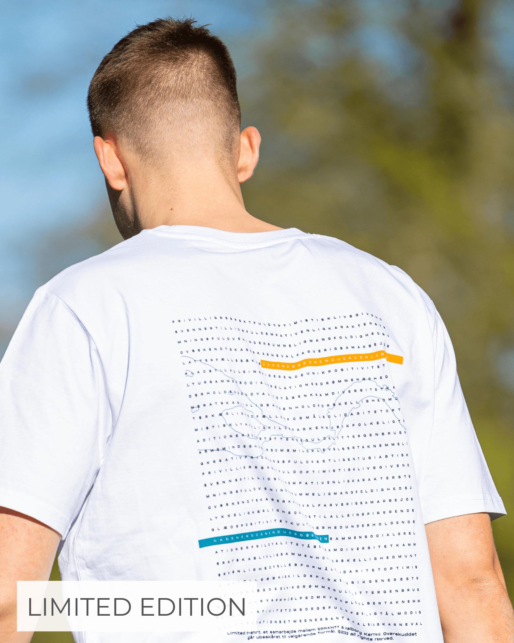 En person iført en hvid T-shirt med et grafisk design på ryggen står udendørs. Teksten "LIMITED EDITION" er synlig i nederste venstre hjørne.