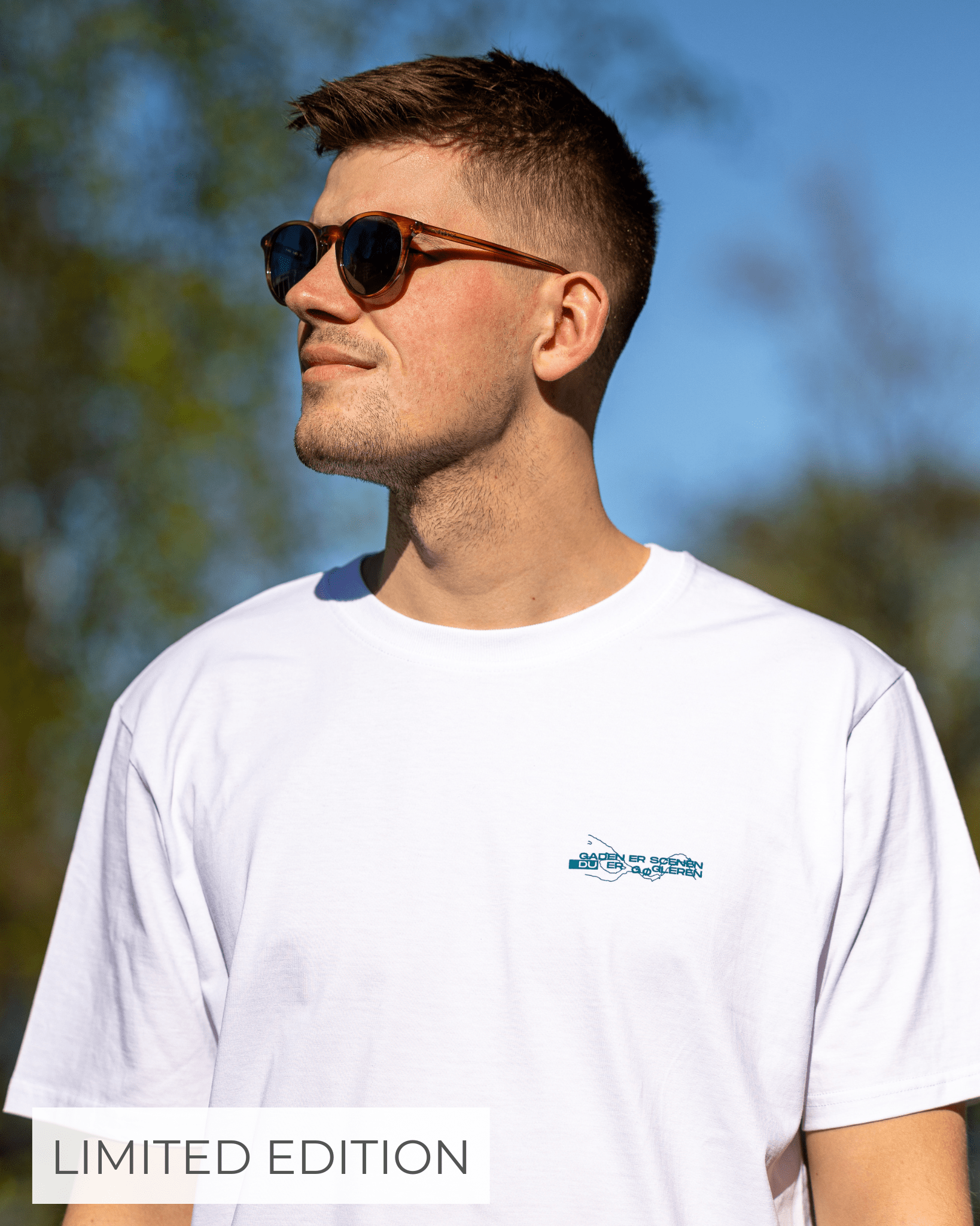 En mand iført solbriller og en hvid t-shirt står udendørs i solskin. Teksten "LIMITED EDITION" er synlig i nederste venstre hjørne.