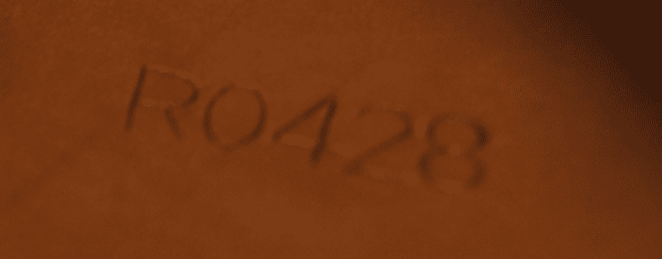 ndgraveret tekst 'RO428' på en brun overflade.