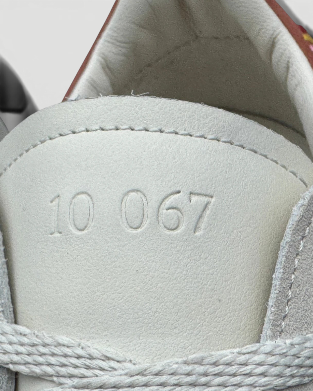 Close-up of the tongue on an Errant Lux Court Sneaker featuring the embossed text 10 067 on off-white premium leather.