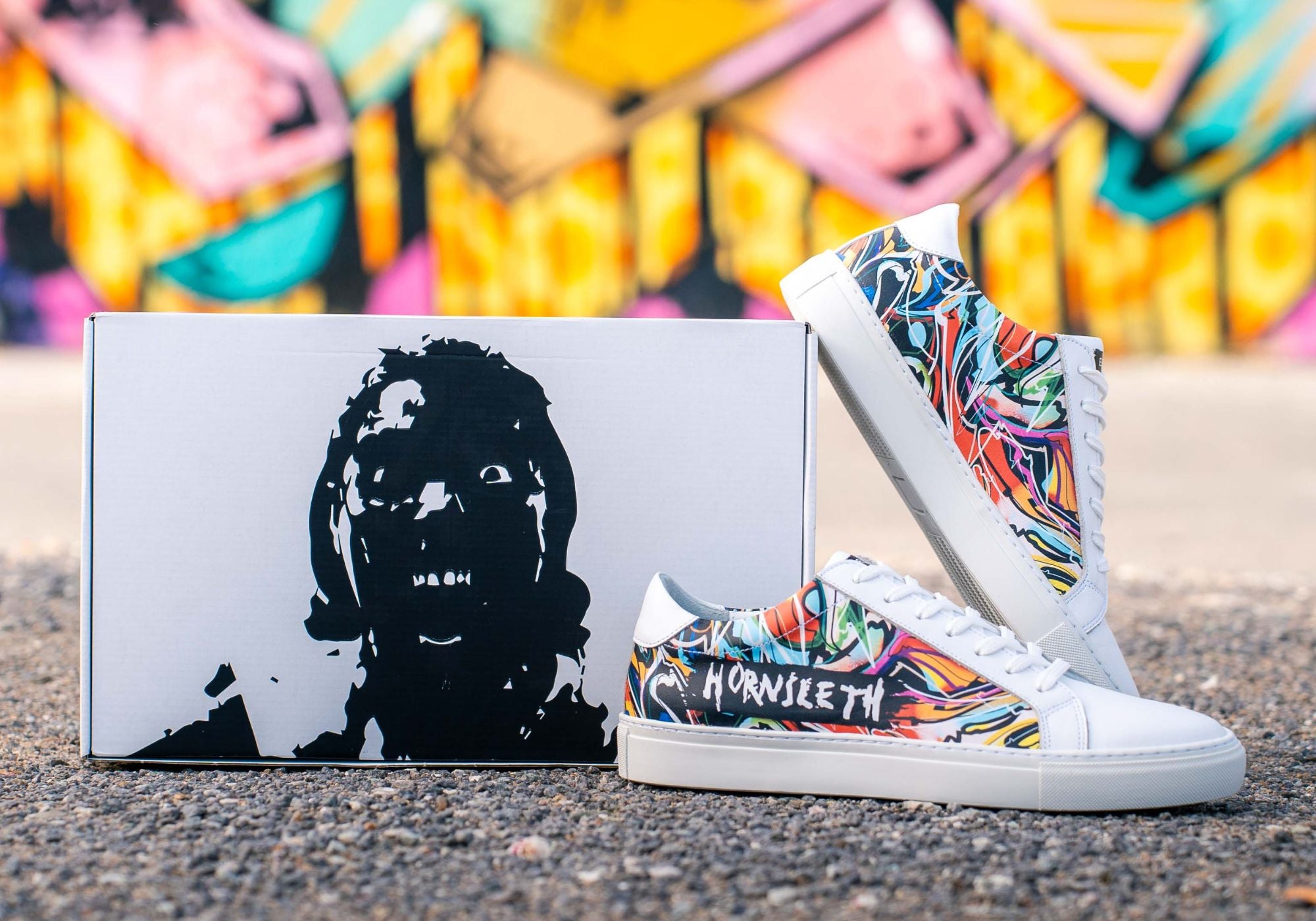 Errant x Hornsleth sneakers står op ad tilhørende kasse med grafiti i baggrunden 