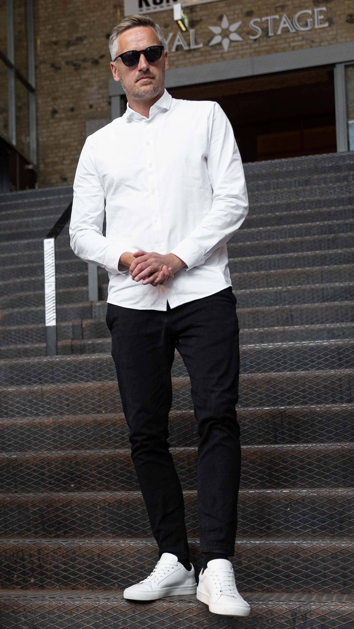 Mand i hvid skjorte og sorte bukser står på trapper.