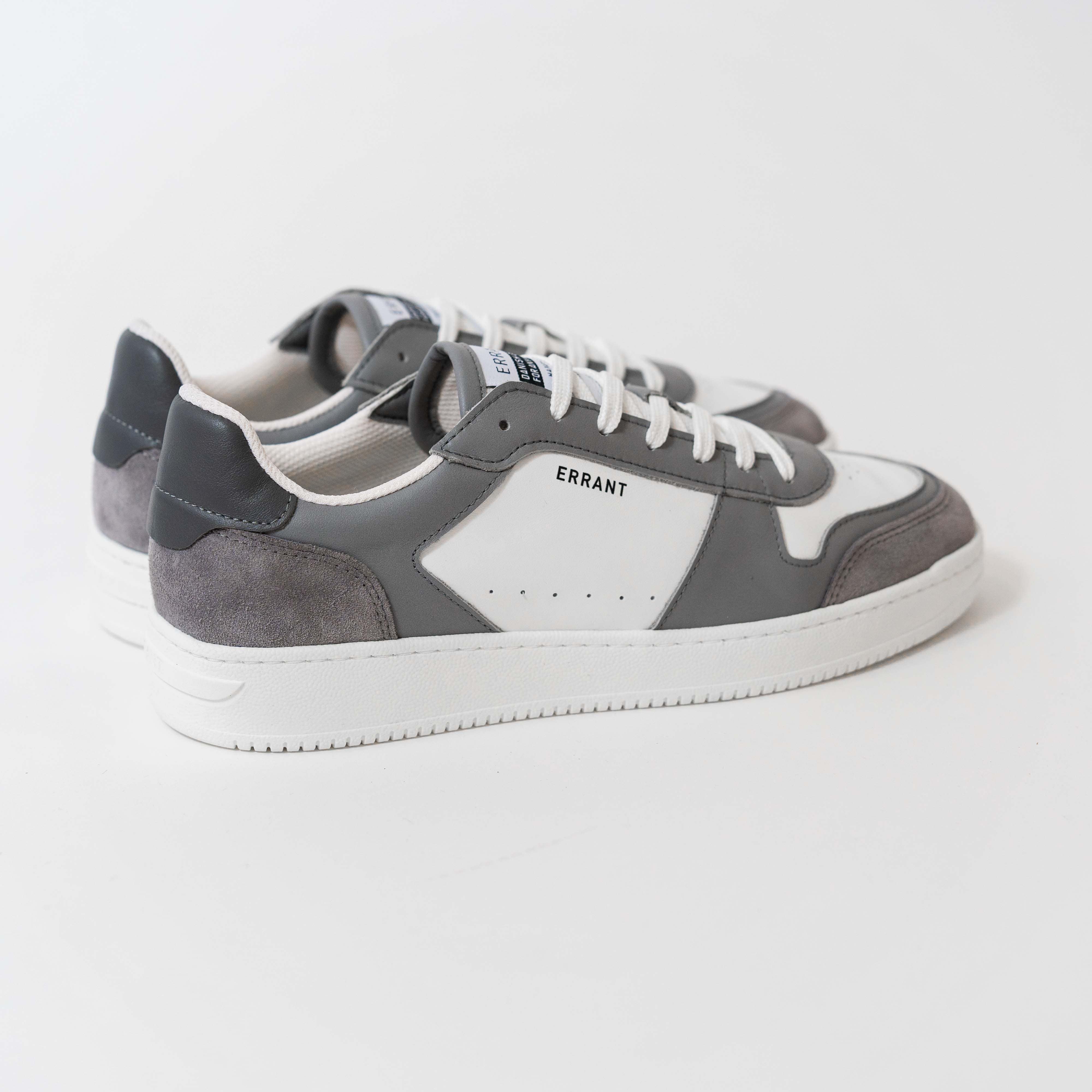 Billedet viser et par grå og hvide sneakers med mærket "ERRANT" på siden. Skoene har hvide snørebånd og en hvid sål.