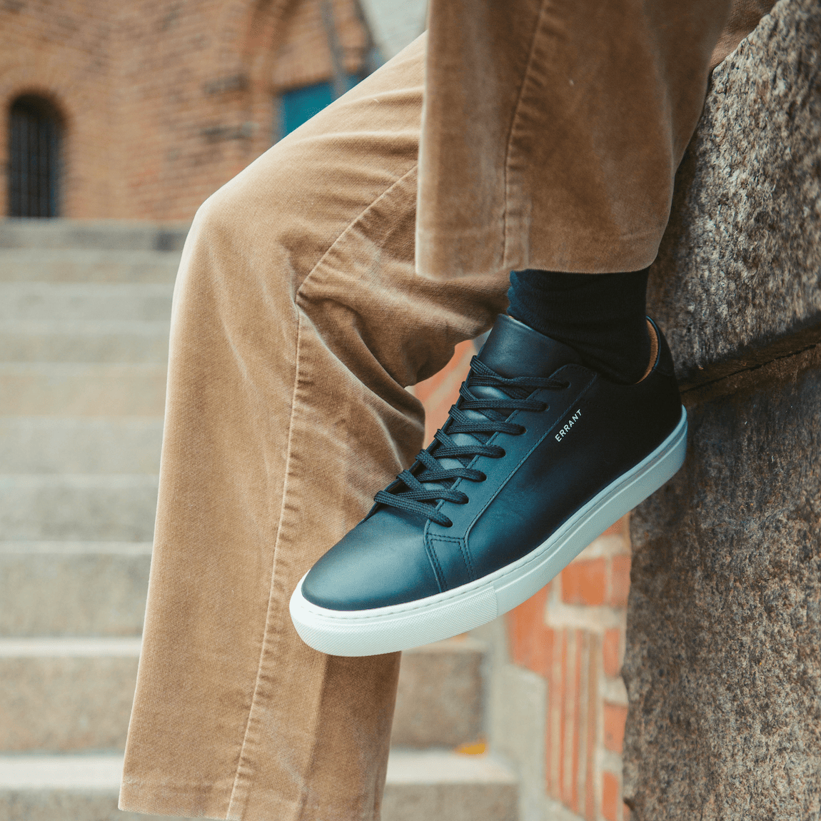 Sort sneaker på personens fod, som sidder på en trappe.