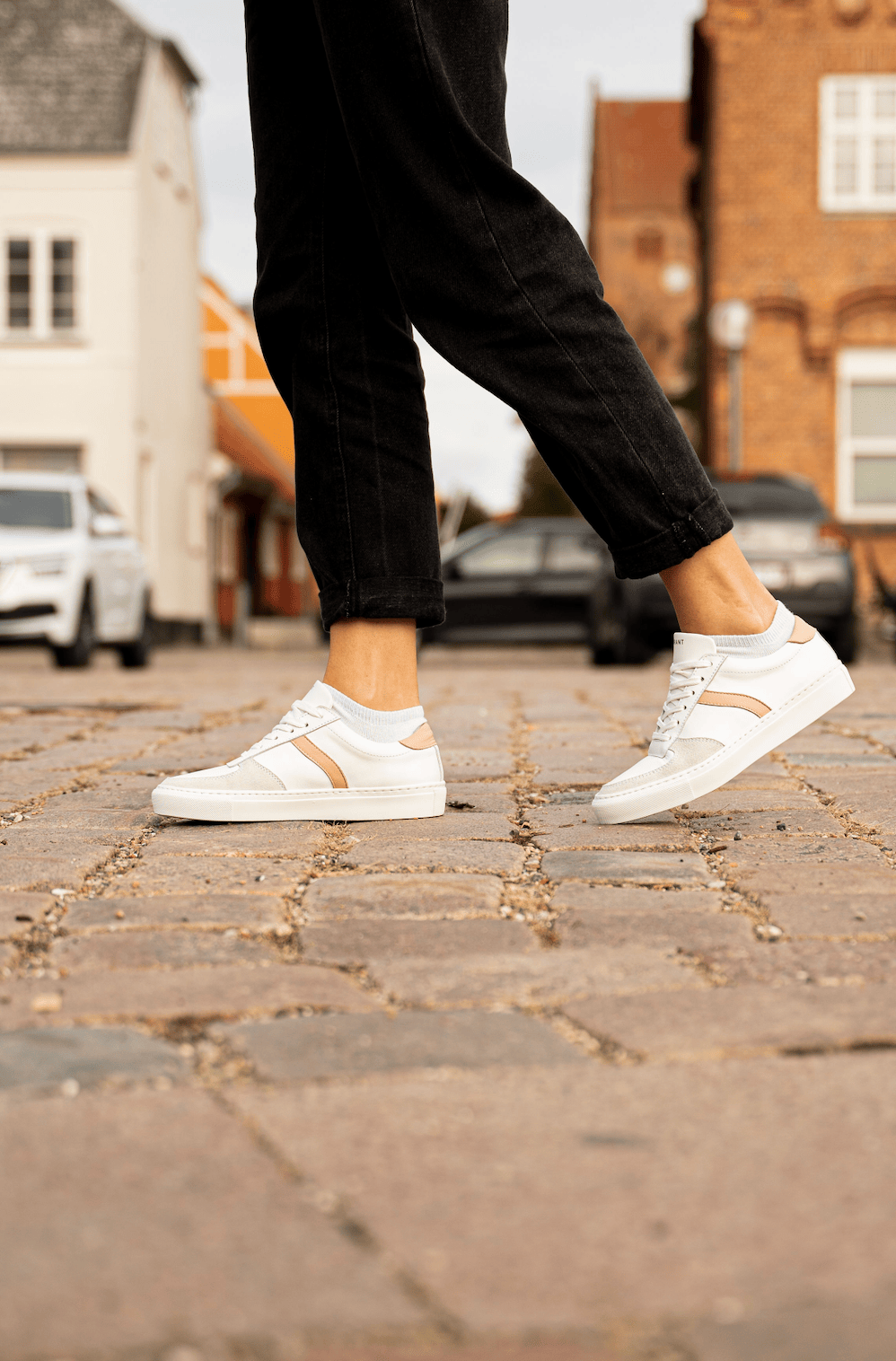 Person iført hvide sneakers går på en brostensbelagt gade.
