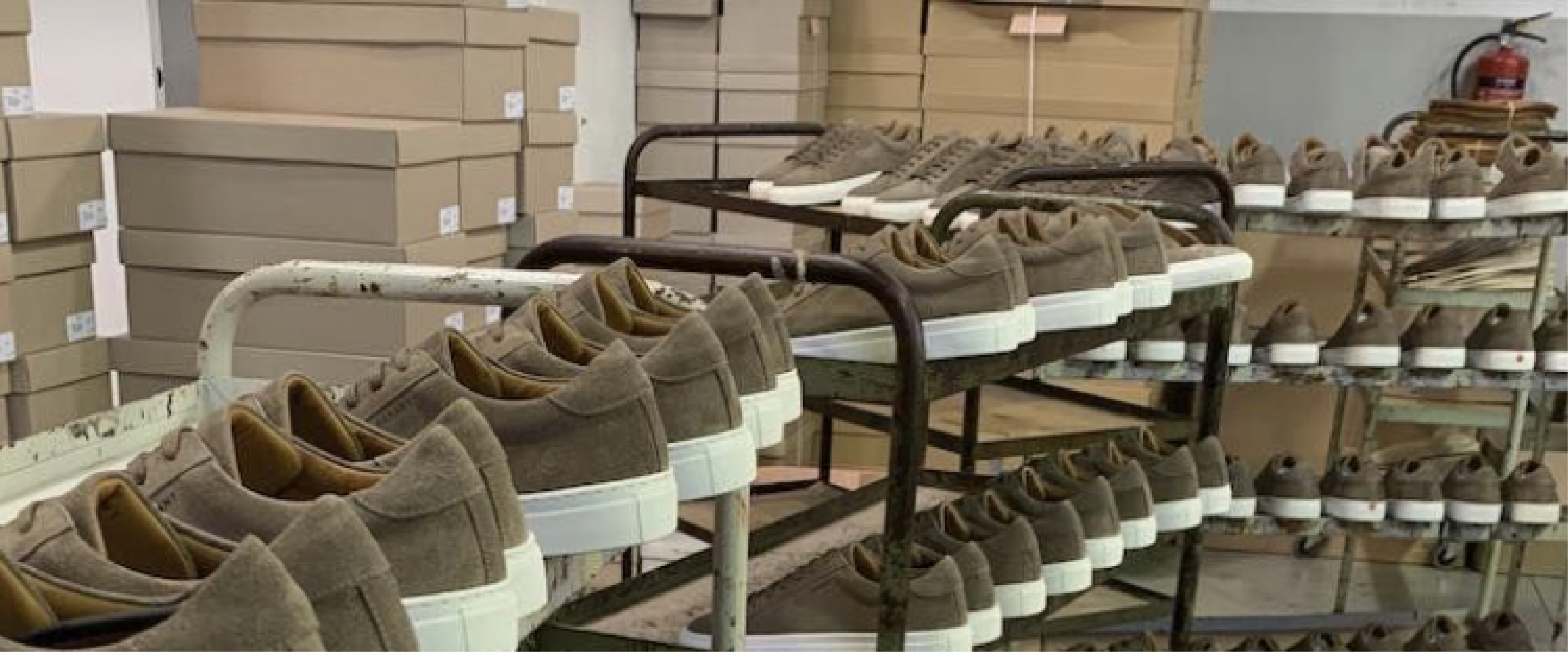 ALT tekst: Rækker af brune sneakers på metalstativer i en fabrik.
