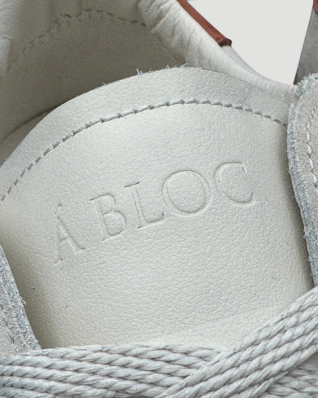 Close-up of the Errant Lux Court Sneaker tongue featuring embossed A BLOC text on off-white leather and suede